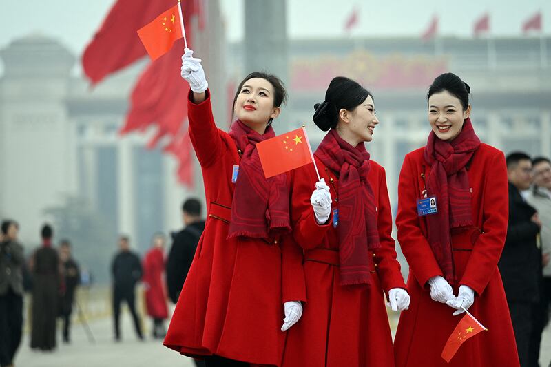 Attendants hold Chinese flags in Tiananmen Square following the closing session of the National People's Congress in Beijing, March 11, 2025.
